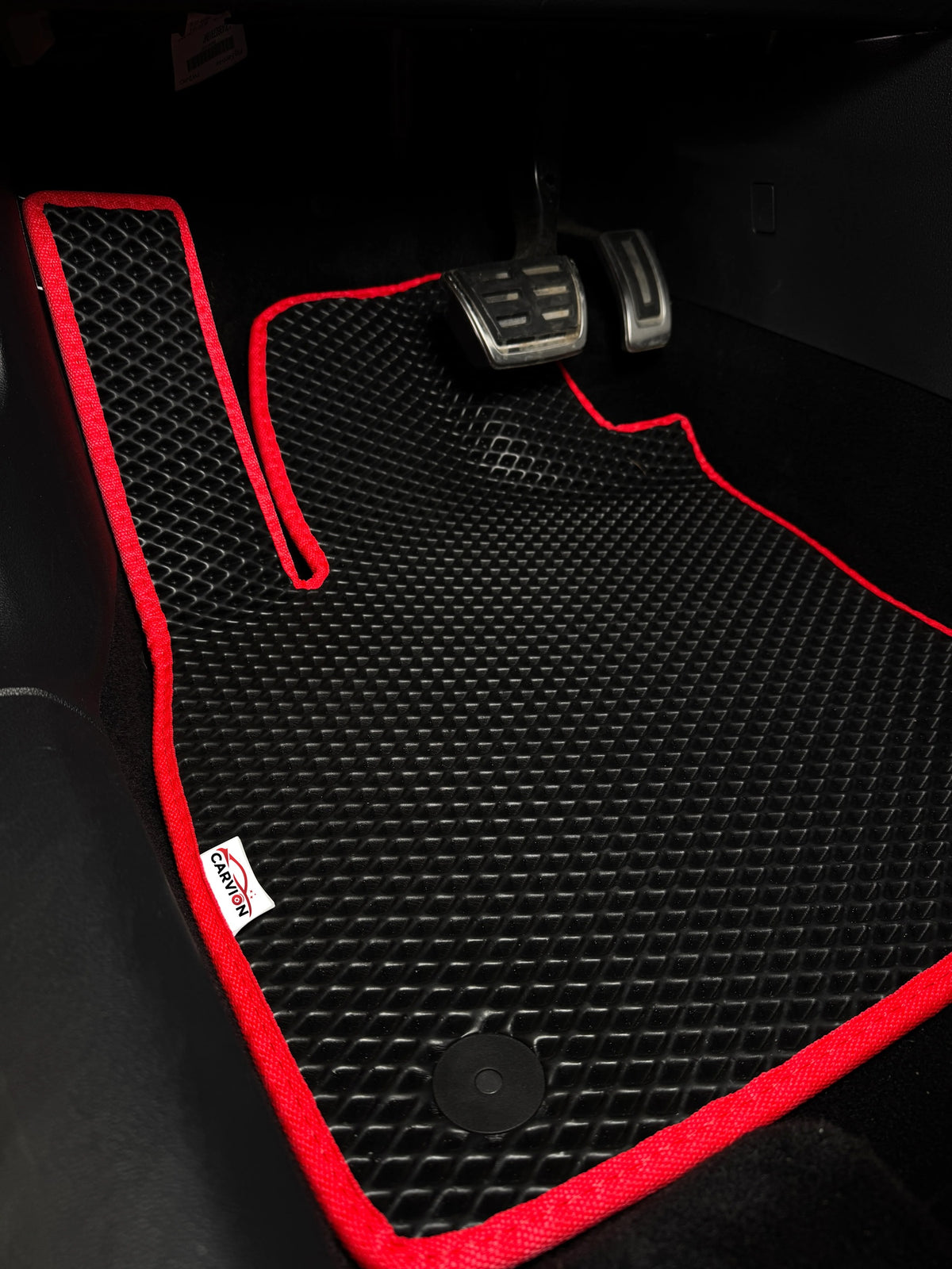 Illustrative photo: black EVA mat without raised edges, with red trim, in the driver's footwell